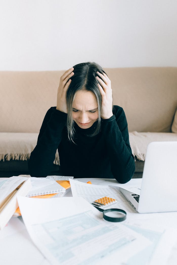 our-story A woman appears stressed and overwhelmed with paperwork at her home desk.