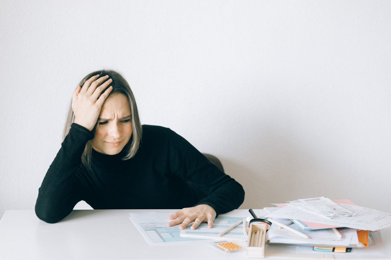 services-01 Woman in black sweater stressed with financial paperwork, overwhelmed at white table.