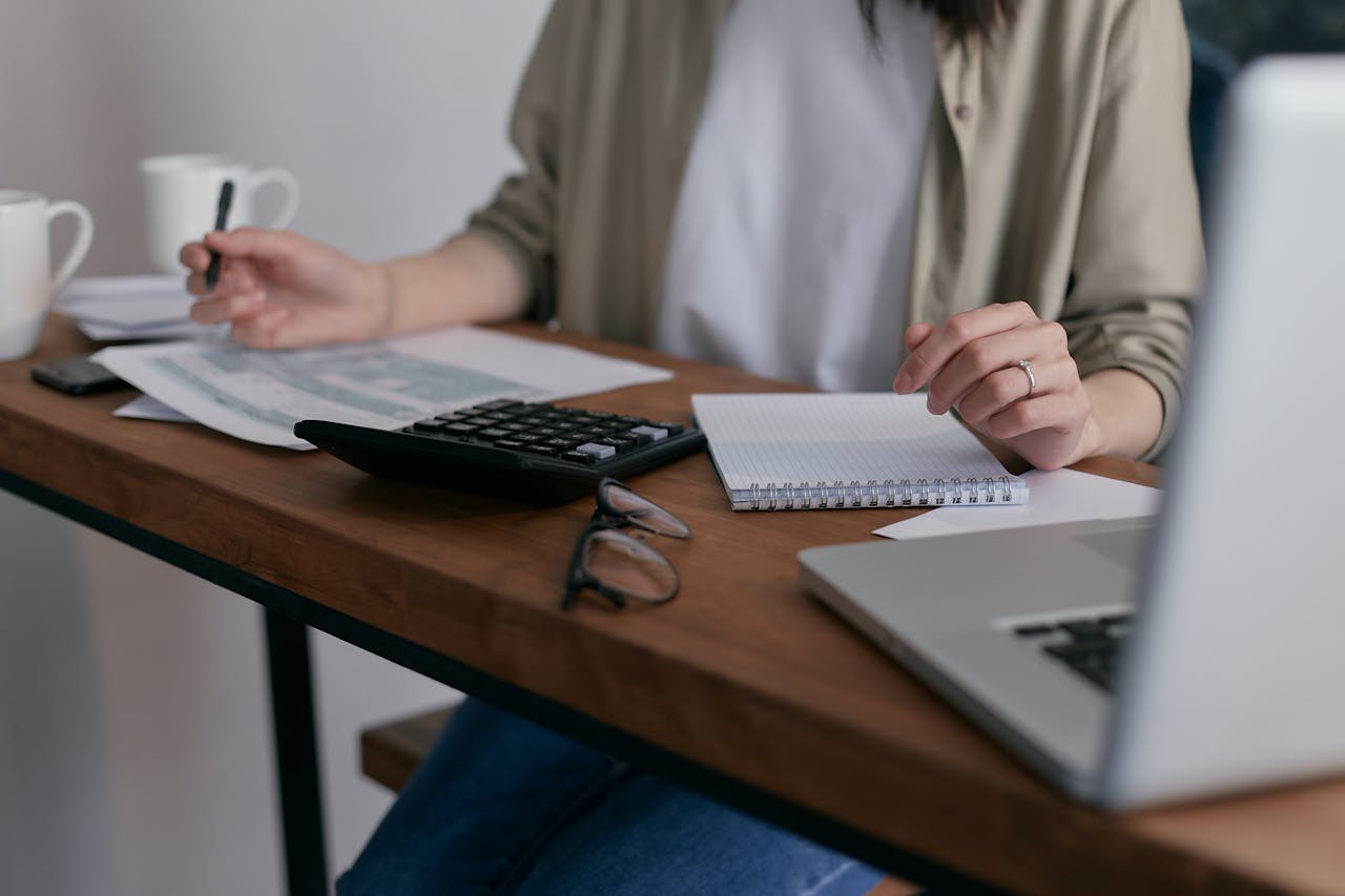 home-hero A woman manages finances at home, using a laptop and calculator on a wooden desk.