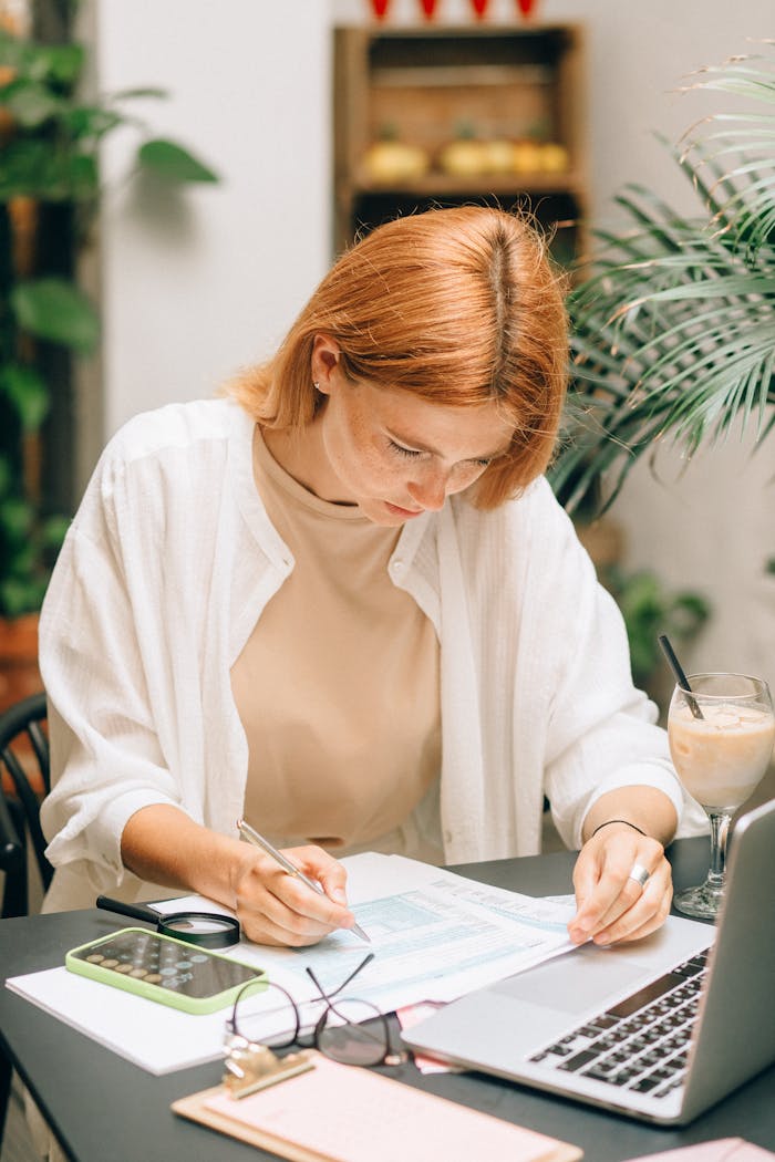 about-bg Woman analyzing financial documents using laptop and calculator indoors.